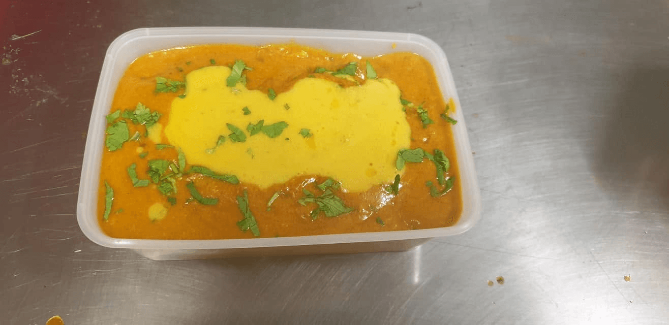 Freshly prepared curry with coriander garnish in a takeaway container